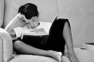 ソファに座って考え込みながら本を読む少年