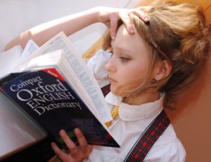 女の子が片腕で頭を抱えて寝ながら本を見ている